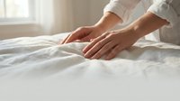 Woman in white shirt touching soft white bedding, testing fabric quality and comfort for home decor, bedroom design, and lifestyle content.