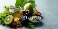 Healthy superfood ingredients with green tea, chia seeds, kiwi, figs and leafy greens arranged on gray surface for nutritious diet and wellness lifestyle.