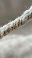 Close-up macro shot of frayed natural hemp rope with loose fibers against soft blurred background. Rustic nautical marine cordage texture detail.