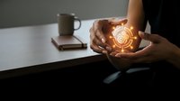 Businesswoman cupping hands around glowing target icon symbol representing goal achievement and strategic planning in modern office workspace.