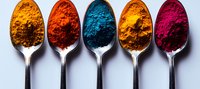 Vibrant natural powder pigments displayed in silver spoons arranged in row showing yellow, red, blue, orange and pink colors against white background. For art and design.
