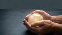 Male hands gently cupping glowing golden orb of light against dark background symbolizing protection, care, energy and spiritual guidance.