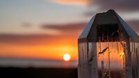 Wooden beach hut with warm glowing light at golden sunset over ocean horizon creating peaceful coastal atmosphere for vacation and relaxation concepts.