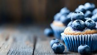 Fresh blueberry muffin topped with ripe berries on rustic wooden table. Homemade bakery with natural ingredients and fresh fruit for healthy breakfast.