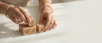 Woman hands arranging wooden cubes with heart symbols on white surface for love concept and romantic decoration projects.