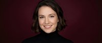 Young professional woman with short brown hair smiling confidently in black turtleneck against burgundy background for business portraits and corporate headshots.