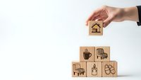 Hand placing wooden block with house icon on pyramid of lifestyle blocks representing home ownership and life balance concept for real estate planning.