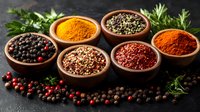 Aromatic spices and peppercorns in clay bowls on dark background with fresh herbs, turmeric, chili powder and scattered black and pink peppercorns.