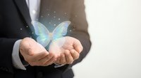 Businessman in formal suit holding glowing holographic butterfly with magical light particles, symbolizing transformation, innovation, and digital technology concepts.
