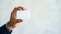Close-up of male hand holding blank white business card against neutral background for corporate branding and marketing purposes.