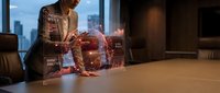 Businessman in brown suit analyzing holographic data analytics interface with glowing digital globe at modern office desk with city skyline view.