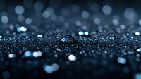 Macro water drop on dark surface with sparkling bokeh lights in blue tones creates atmospheric mood. Artistic nature photography for backgrounds and wallpapers.
