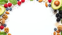Fresh organic superfood ingredients frame with avocado, berries, nuts and seeds on white background. Healthy eating and nutrition concept for wellness.