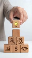 Hand placing wooden cube with lightbulb icon on pyramid of business symbol blocks representing innovation, growth, and strategic planning concepts.
