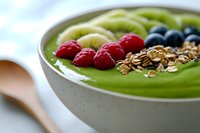 Green smoothie bowl topped with fresh berries, granola and kiwi slices for healthy breakfast nutrition and wellness lifestyle.