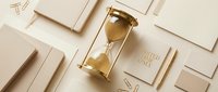 Gold hourglass with flowing sand surrounded by elegant stationery and a limited time only card on a beige background, symbolizing urgency.