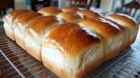 Freshly baked golden dinner rolls arranged in rows on cooling rack, showing soft, fluffy texture and glossy buttered tops. Classic homemade bread for family meals.