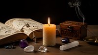 Mystical fortune telling setup with burning candle, open spell book, crystals, wooden chest and smoking incense on dark background for divination.