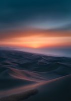 Dramatic sunset over rolling sand dunes creates mystical desert landscape with deep shadows and warm orange light illuminating endless waves of sand beneath dark sky.