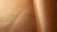 Macro close-up of human skin texture showing natural wrinkles and pores on arm or body surface with warm golden lighting for dermatology and skincare product marketing.