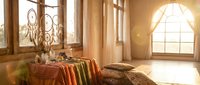 Cozy bedroom interior with warm sunlight streaming through arched windows, featuring ornate bed linens and rustic wooden architecture for home decor.