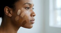 Young African American woman testing foundation makeup shades on face for skincare routine and cosmetic color matching in natural light.