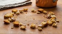 Homemade granola clusters arranged in circle on wooden surface with linen cloth and wooden bowl, overhead flat lay composition for food styling and recipe content.