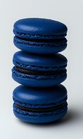 Stack of three blue macarons with dark filling on white background, isolated French pastry cookies for bakery and dessert design projects.