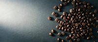 Roasted coffee beans scattered on dark slate surface with dramatic lighting, suitable for beverage packaging, cafe branding, and culinary content.