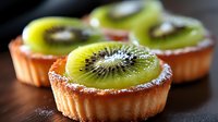 Fresh kiwi fruit tarts with shortcrust pastry and powdered sugar dusting on dark background, close up view of mini desserts for patisserie menu.