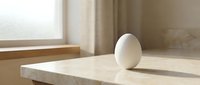 Single white egg on marble countertop in modern kitchen with natural sunlight streaming through window creating soft shadows and warm atmosphere.