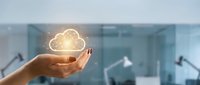 Hand holding glowing cloud computing icon in modern office environment representing digital transformation and data storage solutions.