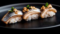 Fresh sea bass nigiri sushi topped with crispy walnuts and microgreens served on black ceramic plate, close up view of traditional Japanese cuisine.