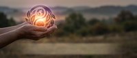 Hands holding glowing orb with sun inside against blurred landscape background, representing renewable energy, sustainability, and environmental conservation concepts.