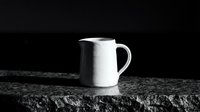 White ceramic pitcher on textured stone surface against dark background, suitable for product mockups, beverage advertising, and kitchen design projects.
