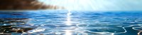 Tranquil ocean surface with sunlight reflection creating shimmering patterns on rippling blue water against dramatic cloudy sky at sunrise.