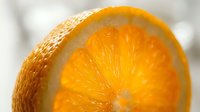 Macro shot of fresh orange slice showing vibrant citrus flesh and textured peel, ideal for food and beverage marketing materials.