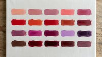 Watercolor paint swatches in warm red pink purple brown tones on textured paper for art supplies color mixing reference and creative projects.