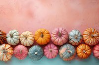 Colorful decorative pumpkins in pastel pink, orange, and blue arranged in row on dual-colored background. Trendy autumn holiday composition with copy space.