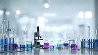 Modern laboratory setup with microscope and colorful chemical glassware on clean white table for scientific research and medical testing applications.