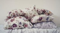 Soft floral pattern pillows and cushions stacked on bed with vintage rose print in purple and pink tones creating cozy bedroom atmosphere.