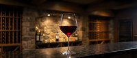 Glass of red wine on bar counter in wine cellar with wooden racks and warm lighting, suitable for wine tasting, hospitality, and beverage marketing.