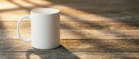 White ceramic mug on rustic wooden table with warm sunlight shadows. Blank coffee cup mockup for custom designs, branding, and promotional materials.