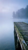Wooden dock extends into calm misty lake surrounded by fog-covered forest trees, creating serene morning atmosphere. Use for travel, nature, wellness, and meditation content.
