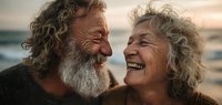 Joyful senior couple laughing together on beach at sunset, showing genuine happiness and love in golden hour light. Retirement lifestyle and relationship goals.