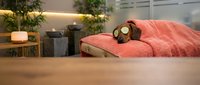 Young woman relaxing in cozy bedroom wearing sleep mask, lying on coral bedding in modern interior with plants and warm lighting for wellness concept.