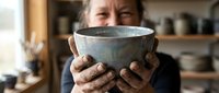 Middle-aged man with weathered hands holding handmade ceramic bowl in pottery studio workshop. Artisan craftsperson displaying clay vessel creation.