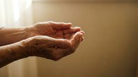 Elderly hands cupped together in prayer or receiving gesture with warm golden light, symbolizing hope, faith, spirituality and compassion in senior care.