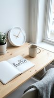 Minimalist home workspace with open notebook, clock, ceramic mug, and plant on a wooden desk by a bright window.