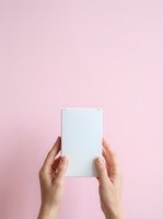 Hands holding blank white card against soft pink background, product mockup for packaging design, branding, marketing materials, and promotional campaigns.